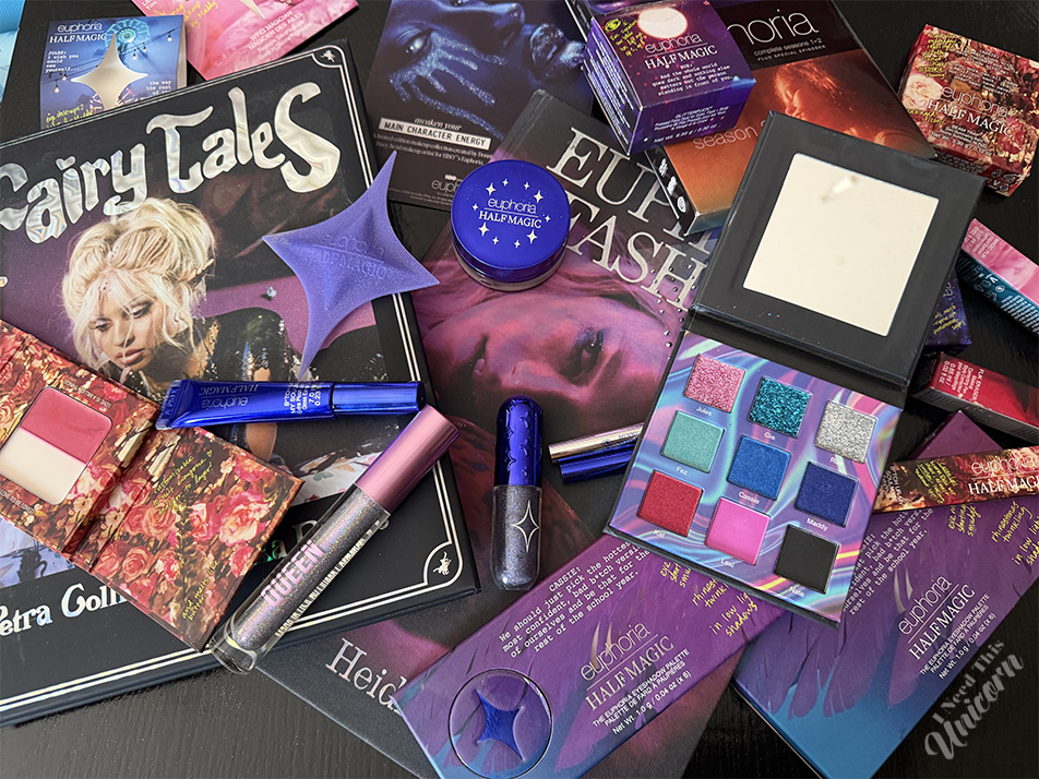 Open colorful Half Magic Beauty eyeshadow palette with Queen Cosmetics neon shimmer shades styled alongside Euphoria-inspired makeup products and fashion books.