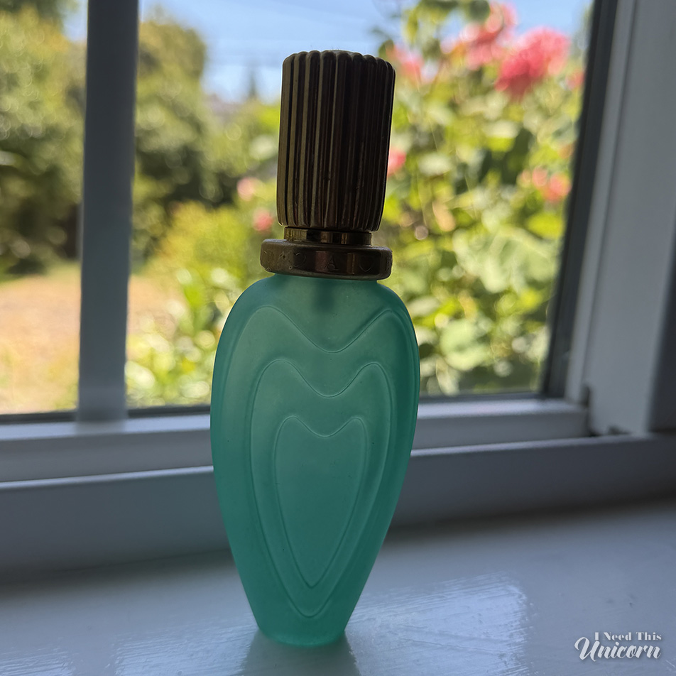 Aqua frosted colored bottle of Escada's Blue Romance sitting on a window sill.