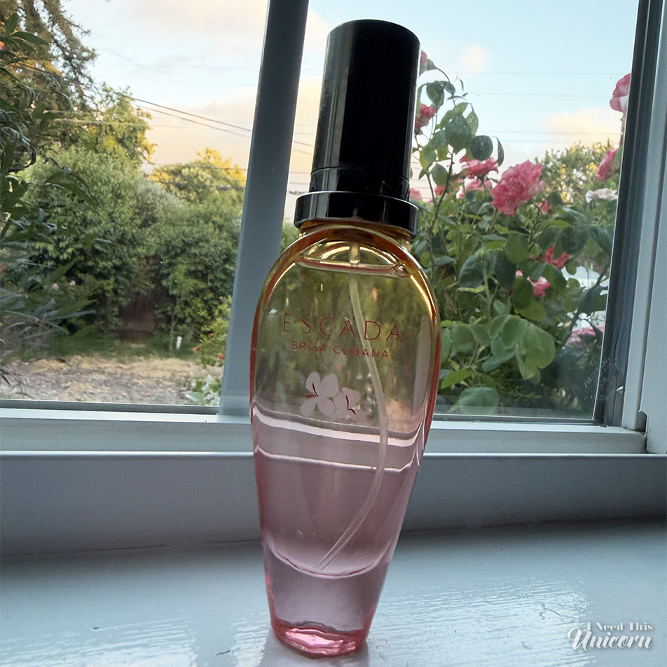 Transparent orange to pink bottle of Escada's Brisa Cubana on a window sill