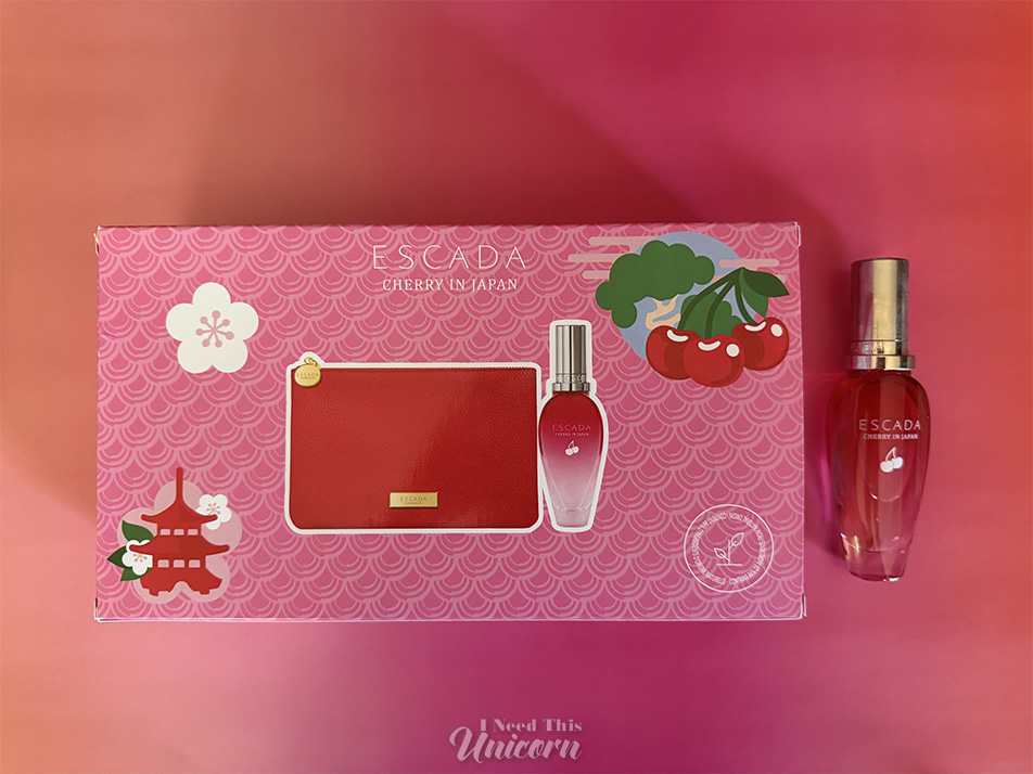 Box and bottle of Escada's Cherry in Japan. Pink box with a red makeup bag, and a red to clear gradient bottle on an orange and pink background.