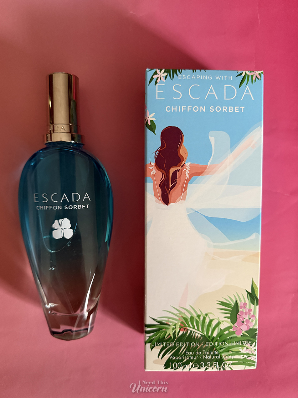 Bottle and box of Escada Chiffon Sorbet on a pink gradient background. The bottle is an aqua to clear gradient with an image of w white flower printed on the front. The box has a vector illustration of a woman with long brown hair and a white gown in a tropical setting.