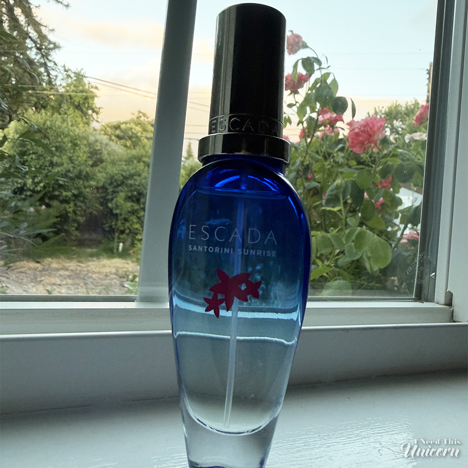 Blue to clear gradient bottle of Escada's Santorini Sunrise on a window sill