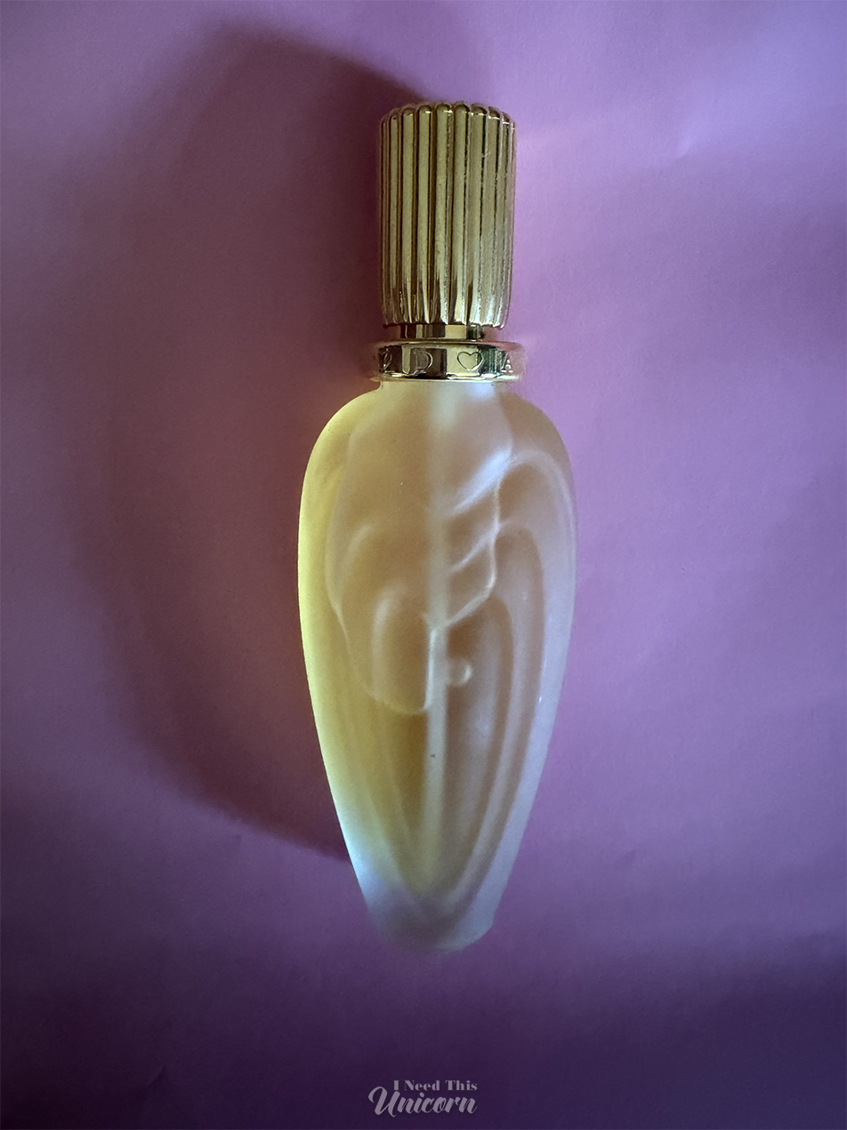 Frosted bottle with yellow liquid of Escada's Tender Light fragrance on a pink (looks lilac- but it's just evening) background)
