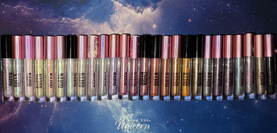 Queen Cosmetics Tester Diamond Shimmer Glosses | I Need This Unicorn Large Queen Cosmetics lip gloss collection arranged in a row on a galaxy-themed background. The collection includes holographic and multichrome glosses in white, pink, lavender, gold, bronze, and black-based shades. Several well-loved tubes show wear from frequent use and are included as comparison references for the new tester shades.