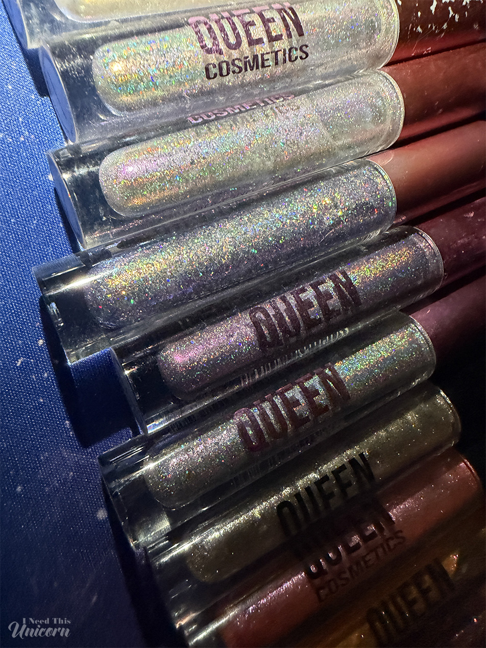 Queen Cosmetics lip gloss collection featuring holographic, iridescent, and multichrome shades with rainbow sparkle and reflective shimmer.