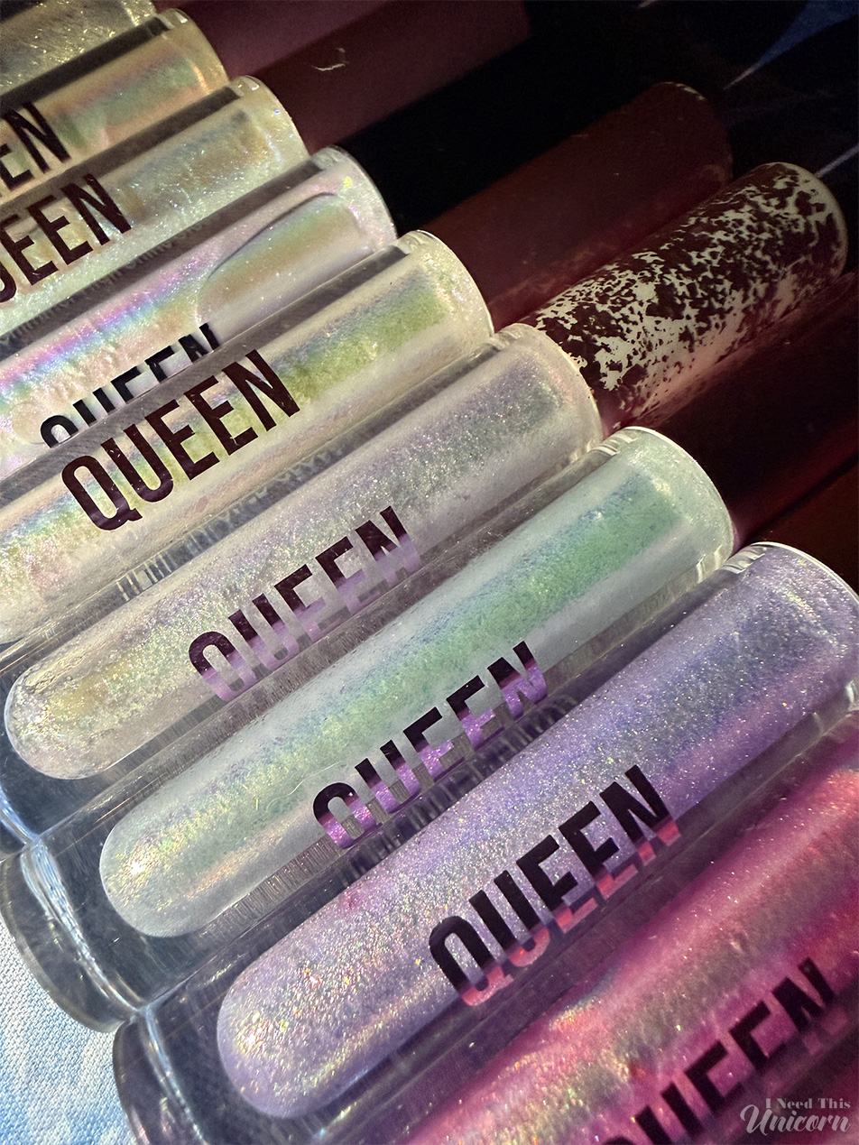 Comparison of three Queen Cosmetics Supernova lip gloss tubes from different points in their lifespan. One heavily used tube appears noticeably lighter than a newer tube, highlighting color shifts that may have occurred due to age, wear, and product contamination.