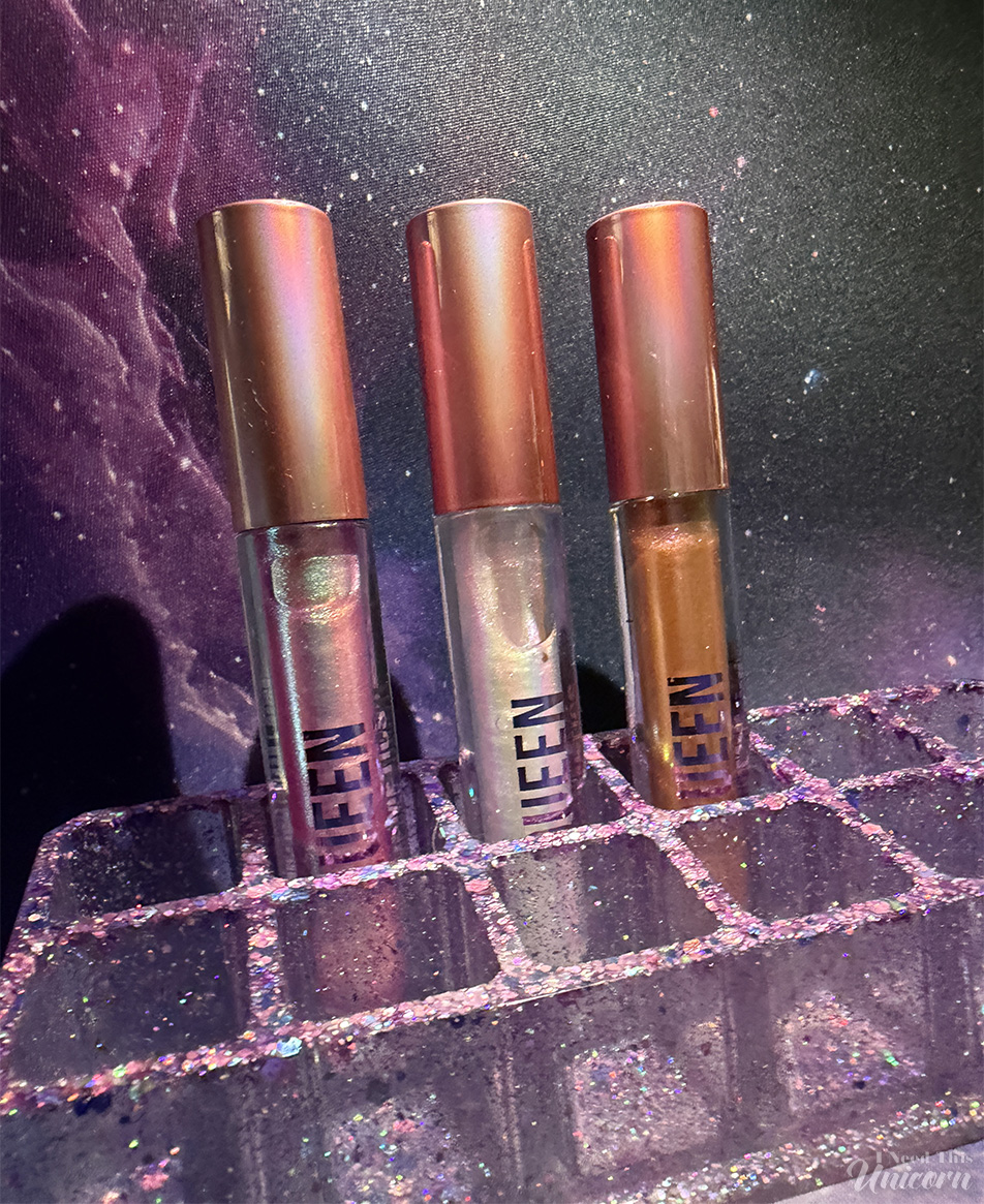 Queen Cosmetics Tester Diamond Shimmer Glosses | I Need This Unicorn Trio of Queen Cosmetics Diamond Shimmer Lip Glosses, in a resin purple glitter lipstick holder by I Need This Unicorn, and a galaxy print gaming mat.
