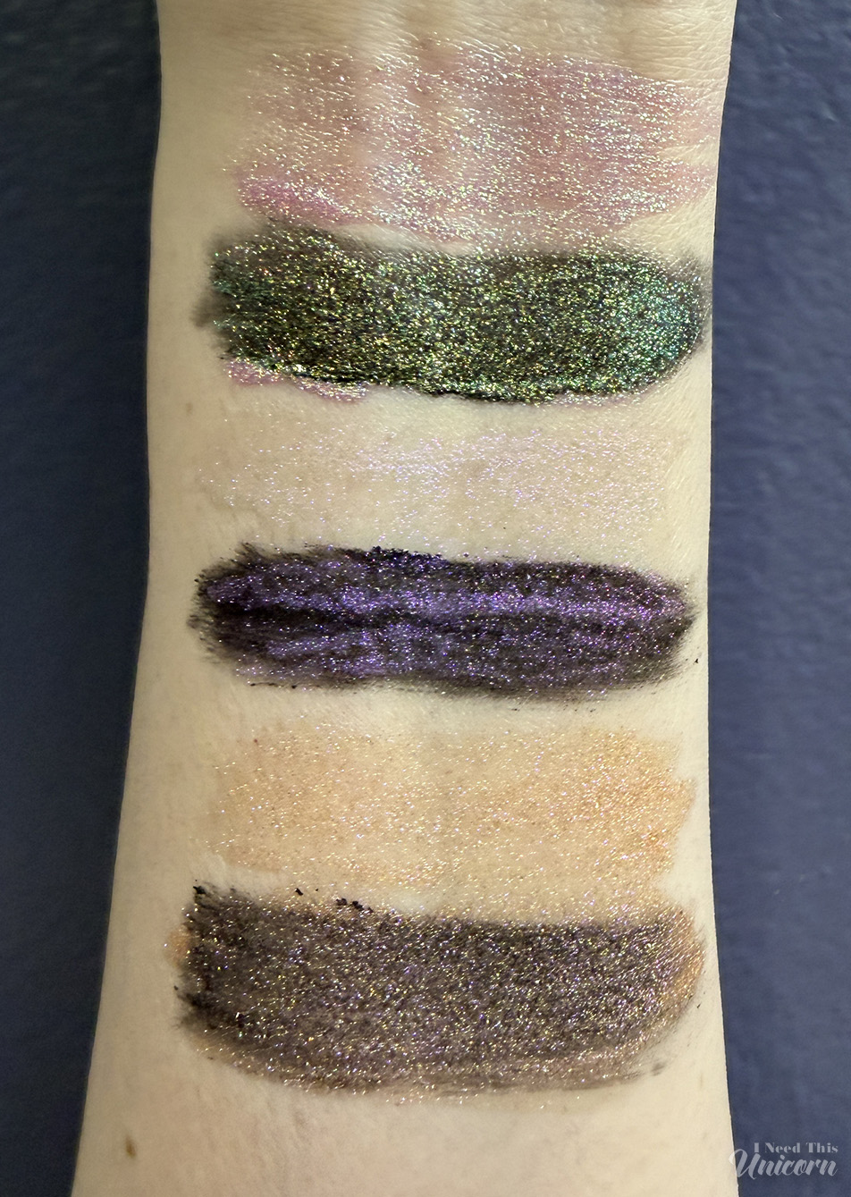 Tester glosses layered over black lipstick and over bare skin, to demonstrate how a dark base enhances the pink, purple, gold, and holographic shimmer effects.