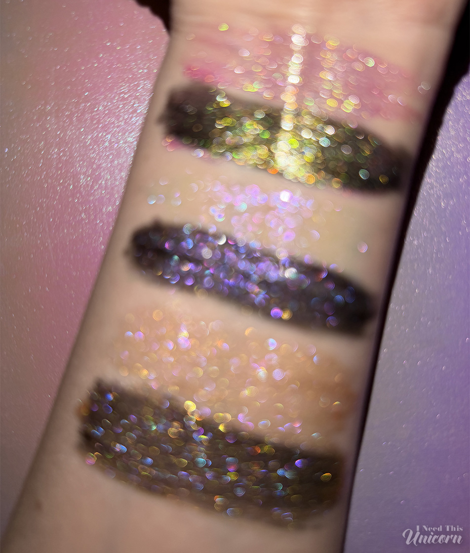 Queen Cosmetics Tester #1, Tester #2, and Tester #3 Diamond Shimmer lip gloss swatches photographed out of focus to show the color shifts in the sparkles. Swatched on bare skin and over black liquid lipstick showing color shifts, and multi-dimensional sparkle.