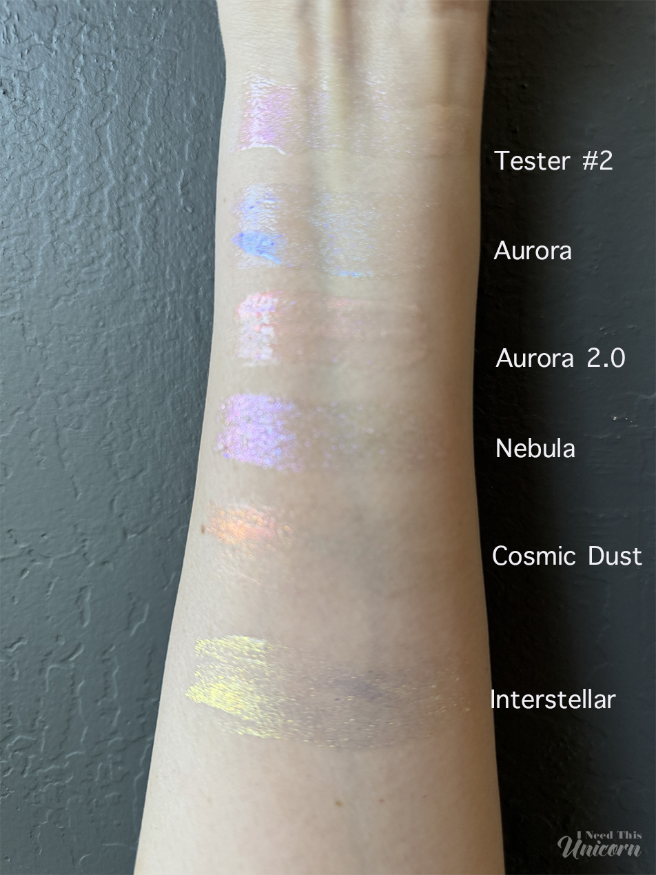 Queen Cosmetics Tester Diamond Shimmer Glosses | I Need This Unicorn Indoor sun light comparison of Queen Cosmetics Tester #2 and five Stardom Collection glosses. Tester #2 displays a soft lavender-pink shimmer, while Aurora shows a blue shift, Aurora 2.0 reflects peach and pink tones, Nebula appears lavender, Cosmic Dust shifts coral and peach, and Interstellar features a gold shimmer.